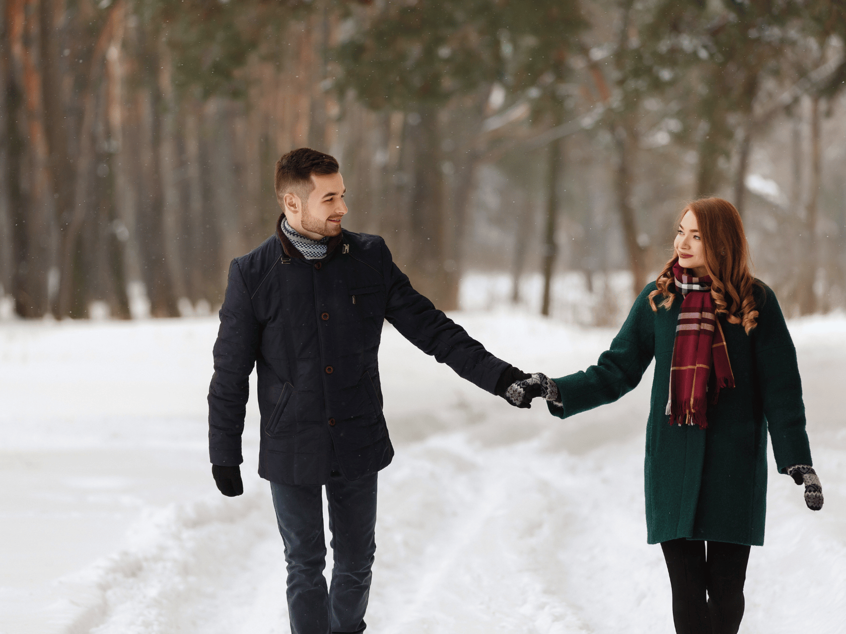 A couple hiking on a snowy trail in the mountains holding hands 