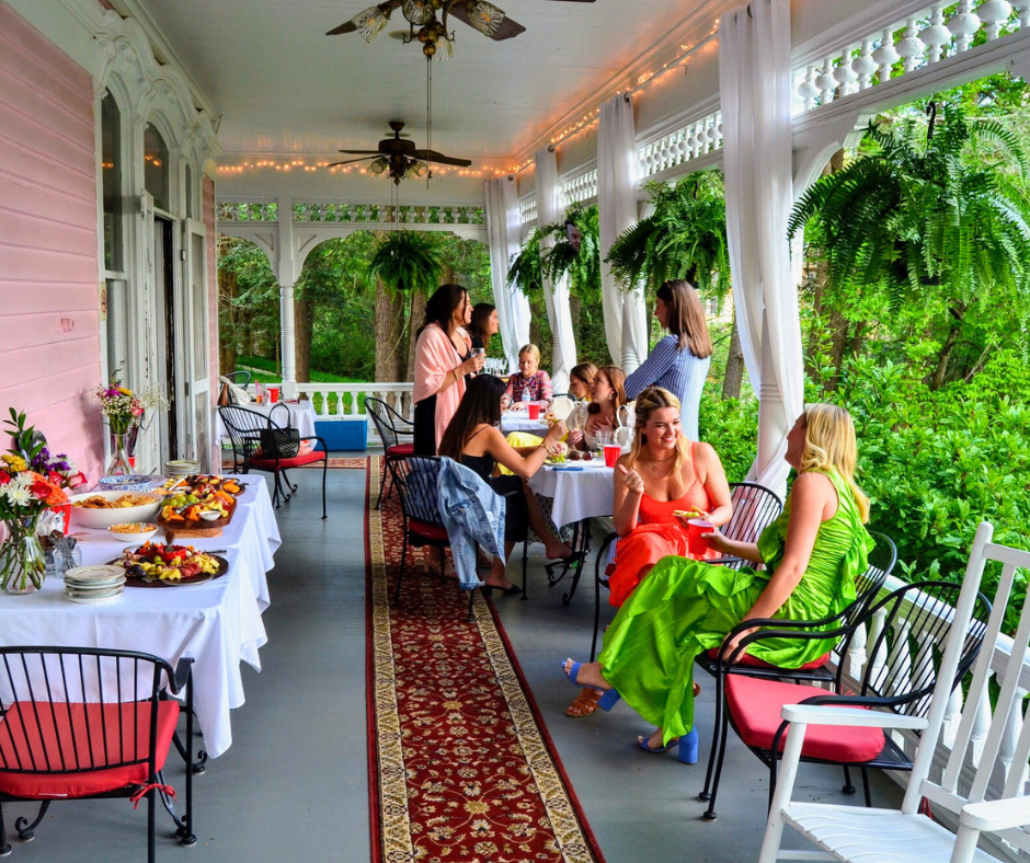 a group of women enjoying a buffest on a wide porch with lush green tress